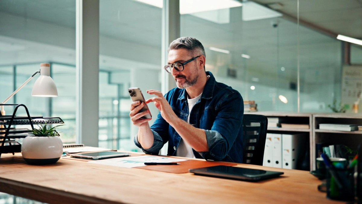 Man at desk in office setting looking at mobile device